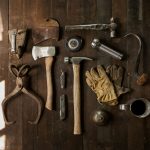 Vintage tools including an axe, hammer, gloves, and metal implements on dark wooden planks