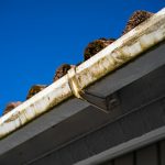 Dirty gutters and roof against a blue sky