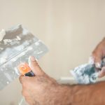 Hands applying plaster to a wall with trowels