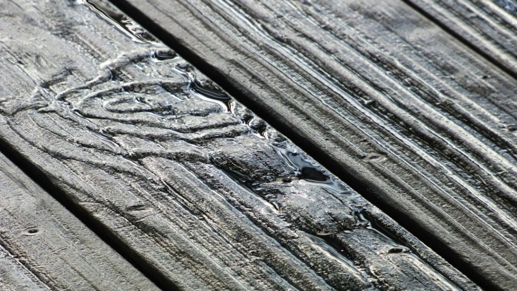 Rainwater pooling in the deep grain of weathered grey wooden deck planks