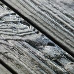 Rainwater pooling in the deep grain of weathered grey wooden deck planks
