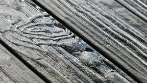 Rainwater pooling in the deep grain of weathered grey wooden deck planks